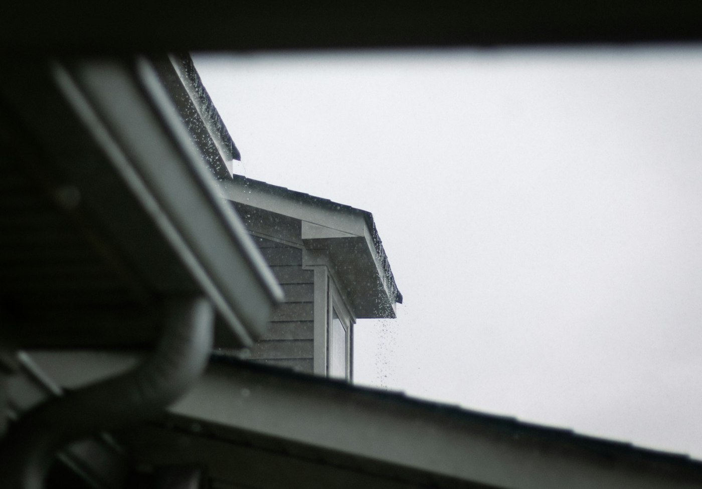 The eave of a house showing the gutter run and roof edge against an overcast sky