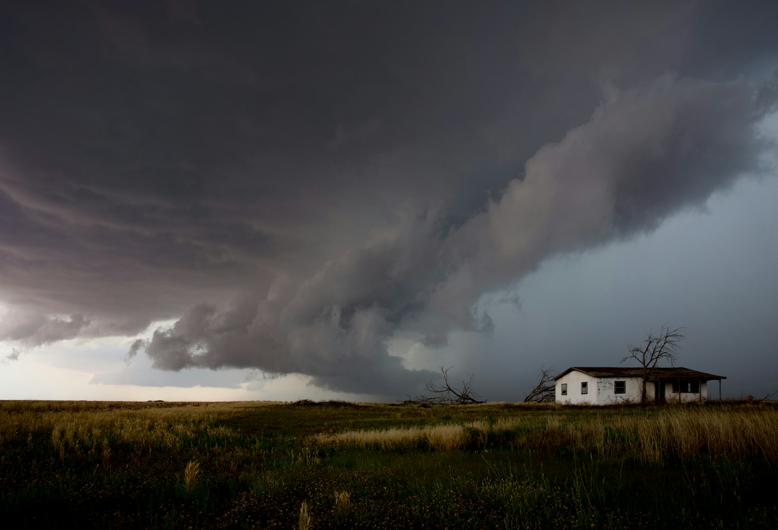 A huge storm cloud and rain band approaching a small house on open land